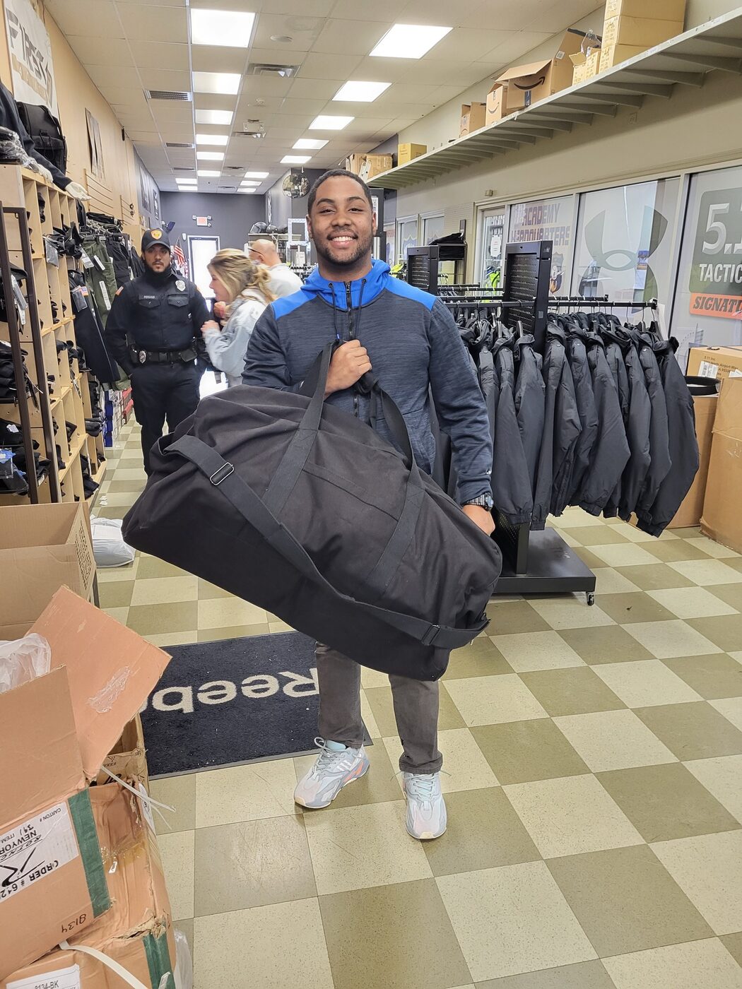 Smiling police academy recruit carrying a garment bag through the Atlantic Uniform showroom